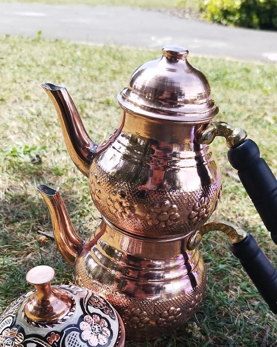Hammered copper two-tier teapot and a sugar bowl with a decorated lid, on the grass